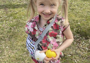 dziewczynka trzyma znalezione w ogrodzie kolorowe jajko